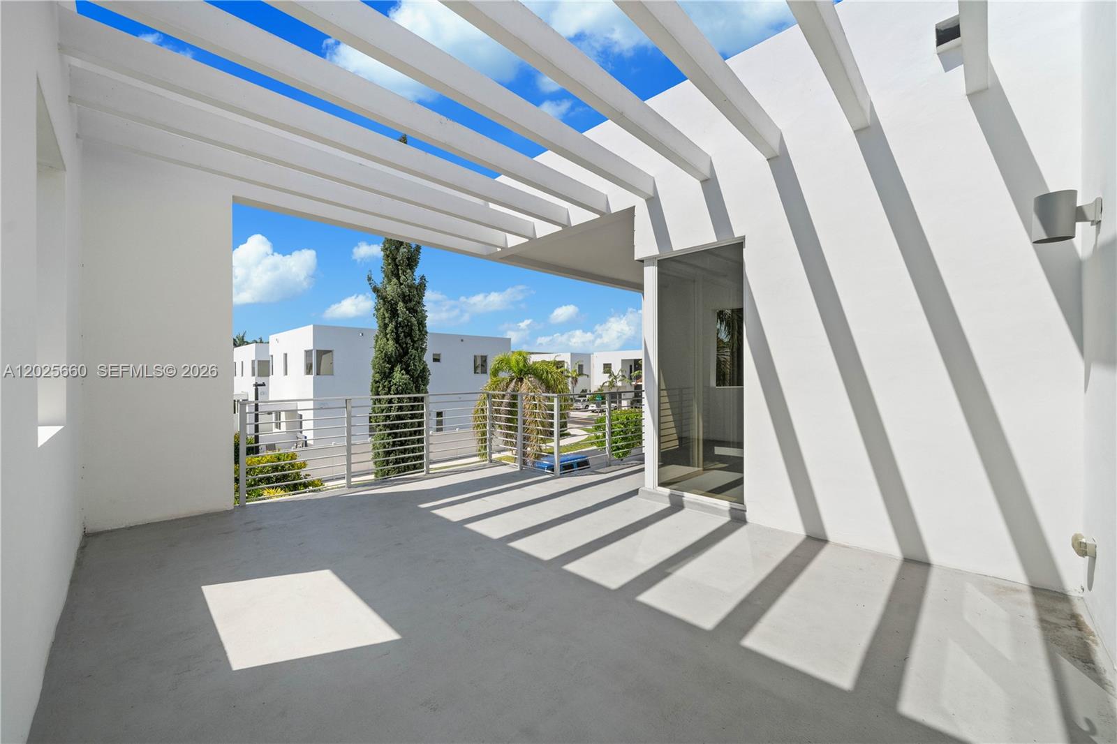 A modern, white-walled balcony features a slatted pergola roof and a metal railing — 9915 NW 75th St, Doral FL 33178, DORAL, FL