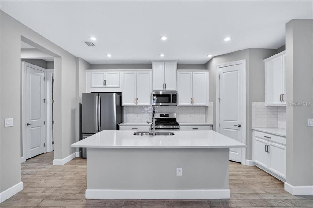 A modern kitchen features white cabinetry, stainless steel appliances, a central island, and tile flooring — 4642 CRESTPOINT WAY, PALMETTO, FL