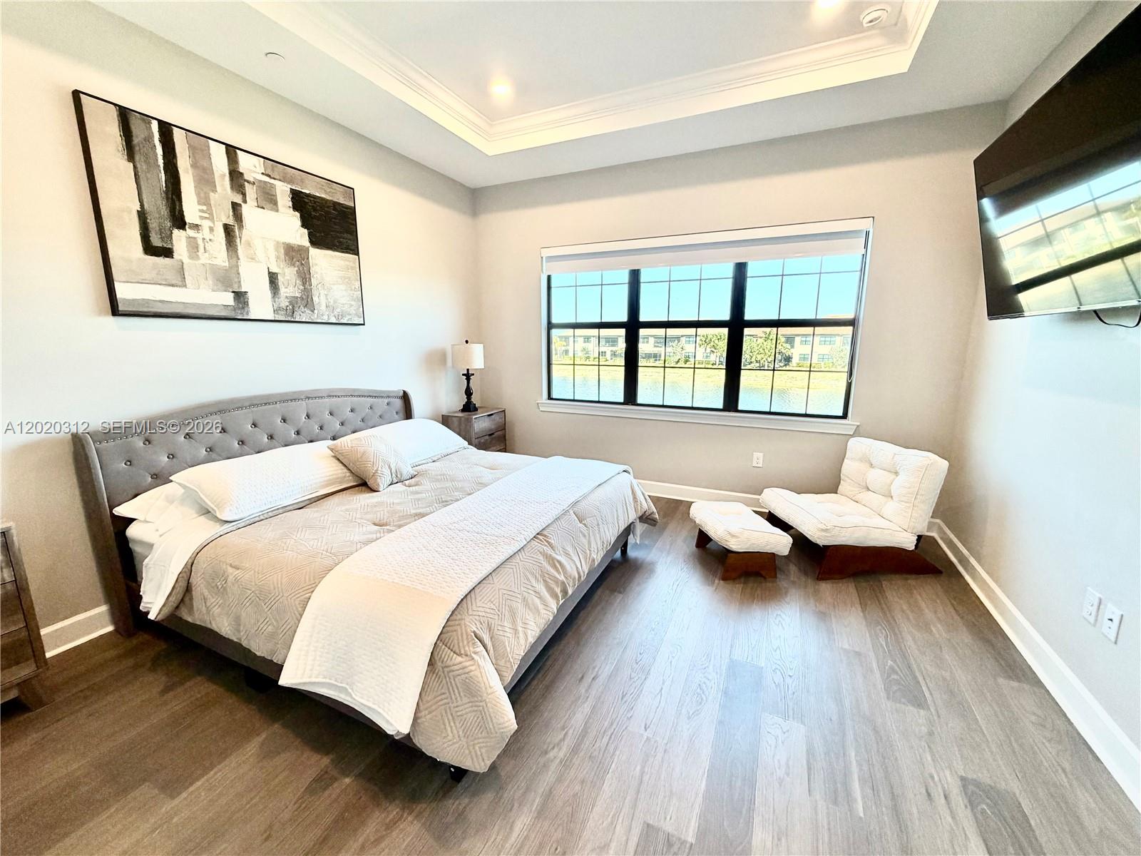 A bedroom features a tufted gray bed, a white lounge chair, and a lake view — 15323 Lucerna # 204, Naples FL 34114, NAPLES, FL
