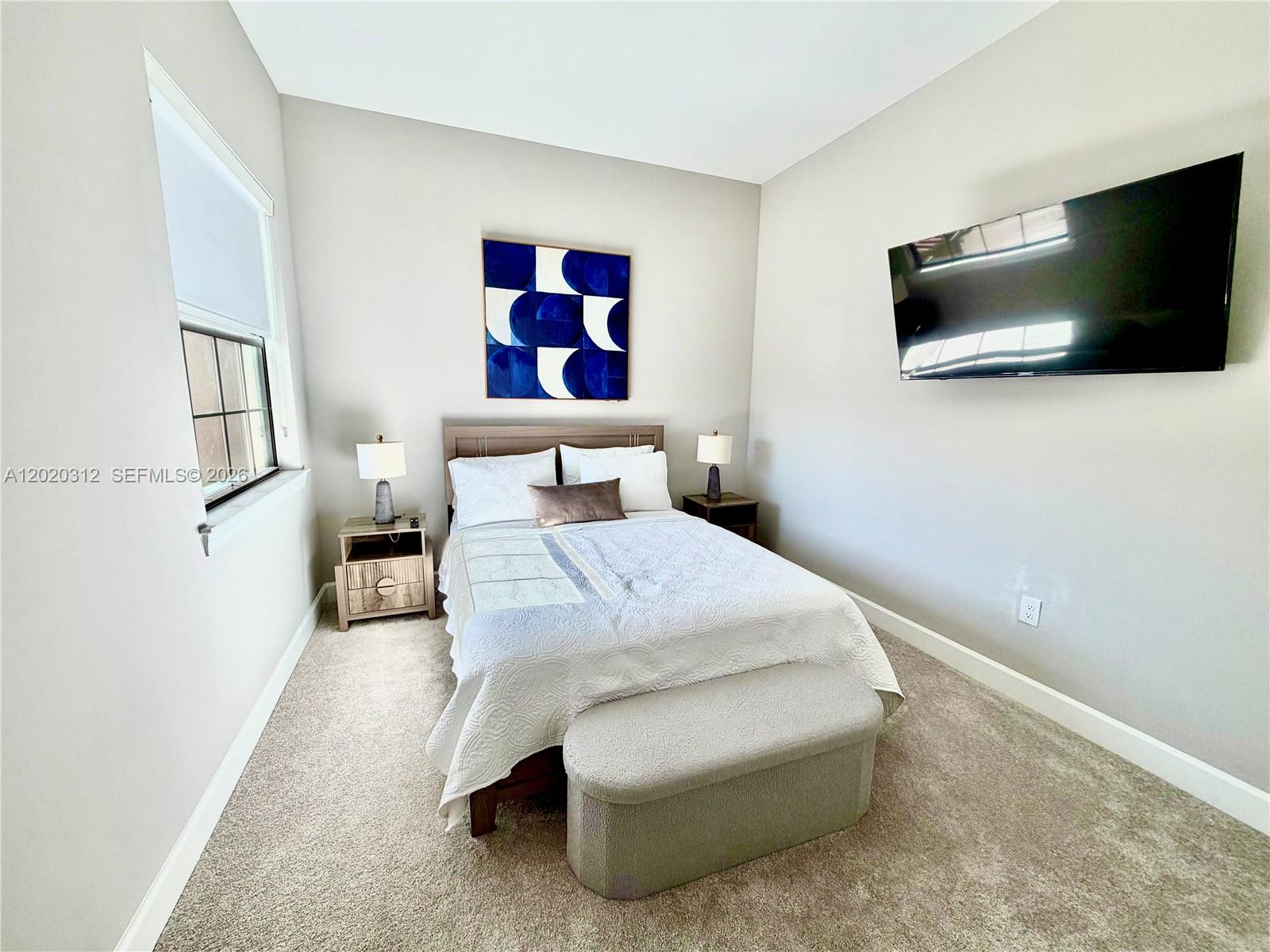 A bedroom features a bed with a blue abstract painting above it and a television — 15323 Lucerna # 204, Naples FL 34114, NAPLES, FL