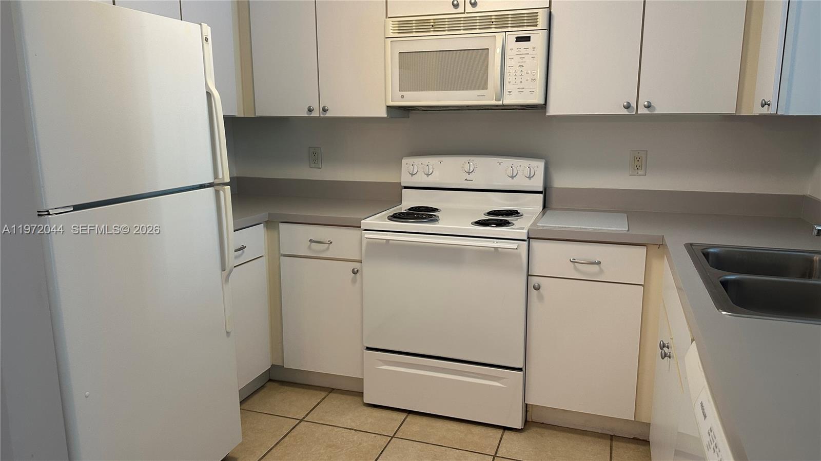 A kitchen features white appliances, white cabinets, a grey countertop, and tan tile flooring — 1250 S Miami Ave # 1012, Miami FL 33130, MIAMI, FL