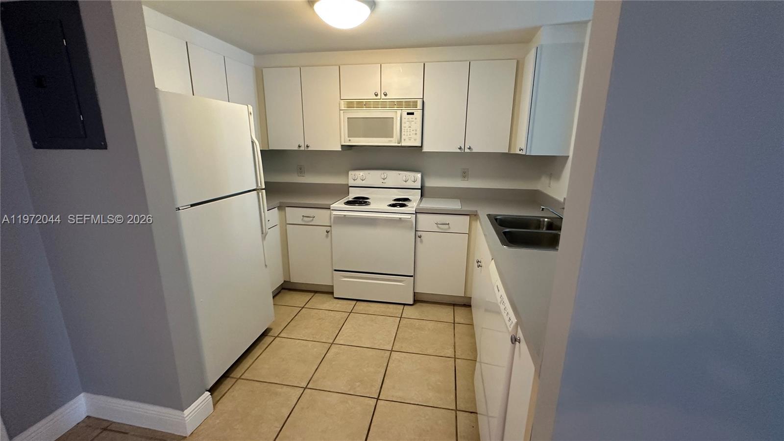 A galley kitchen features white cabinets, white appliances, and light-colored tile flooring — 1250 S Miami Ave # 1012, Miami FL 33130, MIAMI, FL