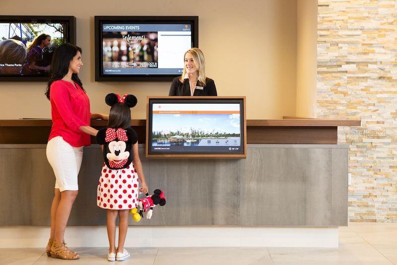 A woman and a child stand at a hotel reception desk with digital displays — 14501 GROVE RESORT AVENUE UNIT 2527, WINTER GARDEN, FL