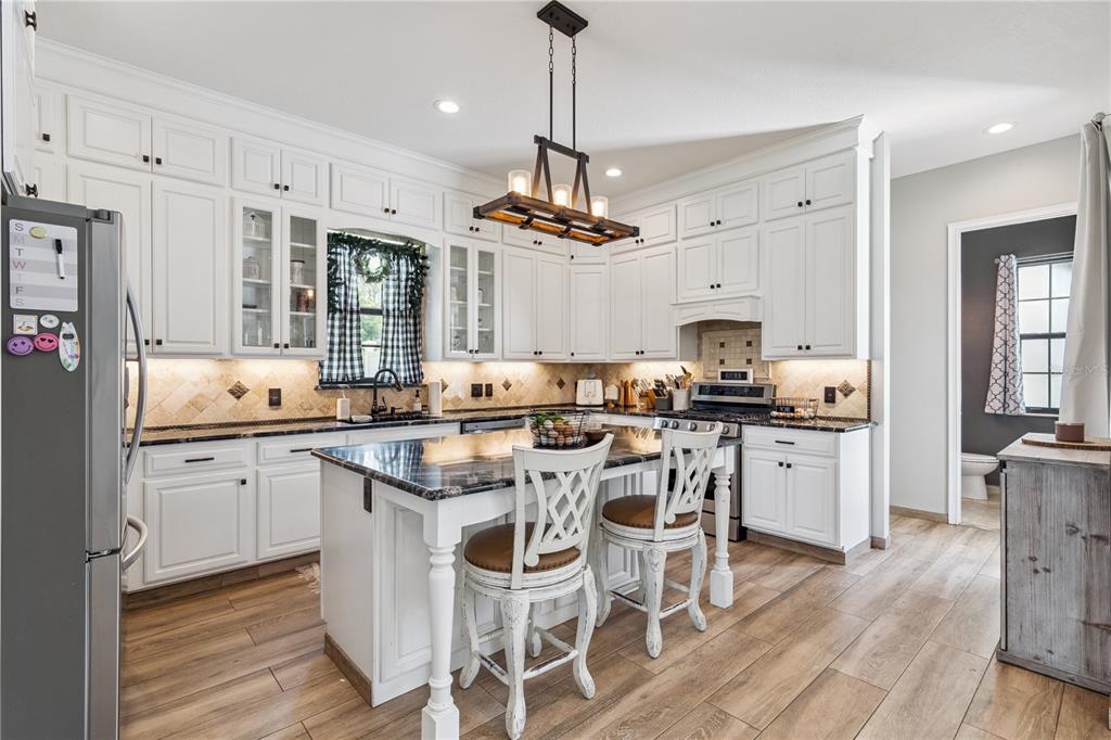 A kitchen features white cabinets, dark granite countertops, a central island, and wood-look flooring — 345 CYPRESS ISLES ROAD, OSTEEN, FL