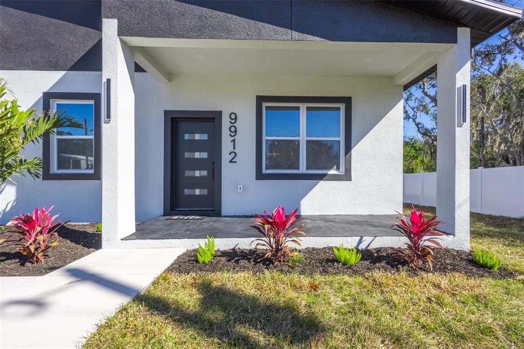 The exterior of a modern house features a dark front door, white stucco walls, and landscaping — 9912 GOLDEN LOOP, NEW PORT RICHEY, FL