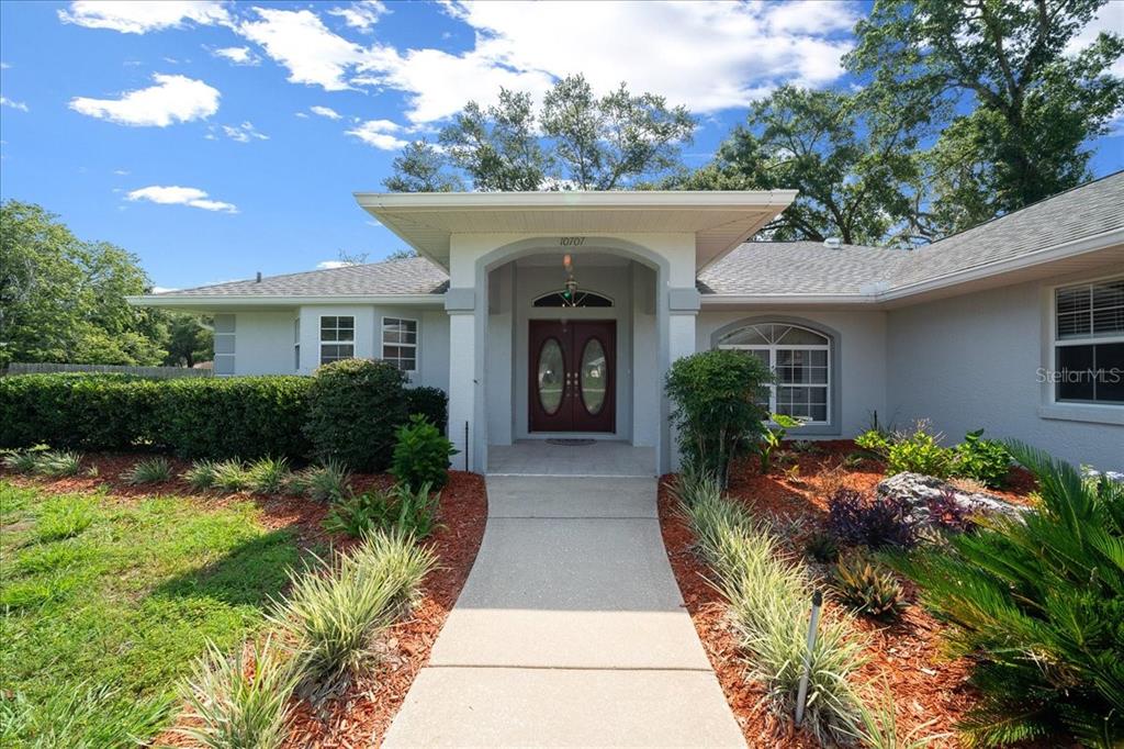 A concrete walkway leads to the front entrance of a single-story house with gray siding — 10707 SW 74TH AVENUE, OCALA, FL
