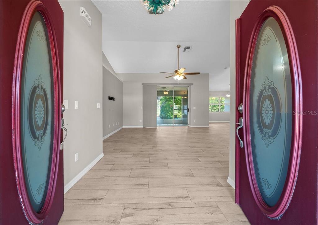 A view through open red double doors into a living room with light wood flooring — 10707 SW 74TH AVENUE, OCALA, FL