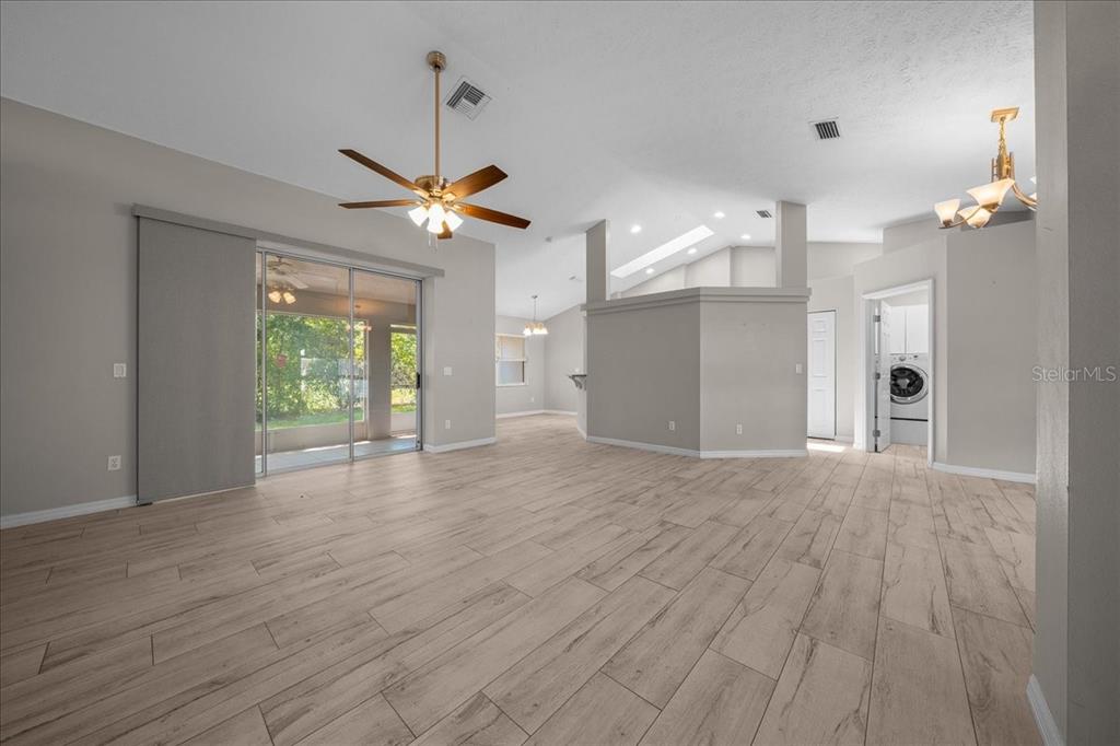 An open-concept living area features light wood-look tile flooring, a ceiling fan, and sliding doors — 10707 SW 74TH AVENUE, OCALA, FL
