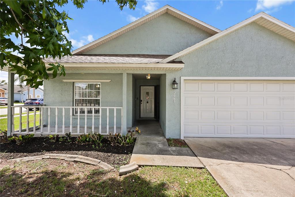 A light green house features a front porch, a single-car garage, and a concrete walkway — 2965 COOL BREEZE CIRCLE, ST CLOUD, FL