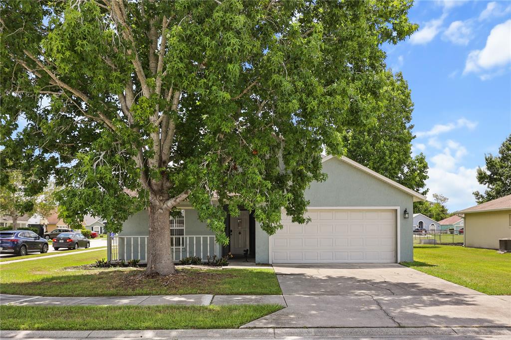 A single-story house with a two-car garage, a front porch, and a large shade tree — 2965 COOL BREEZE CIRCLE, ST CLOUD, FL