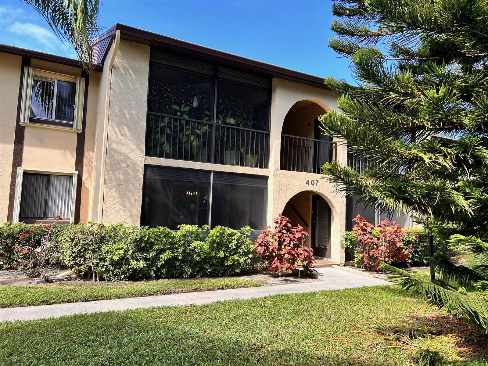 A two-story apartment building exterior features screened balconies, arched entryways, and landscaped shrubbery — 407 Pine Glen Lane # 1, FL 33463, FL