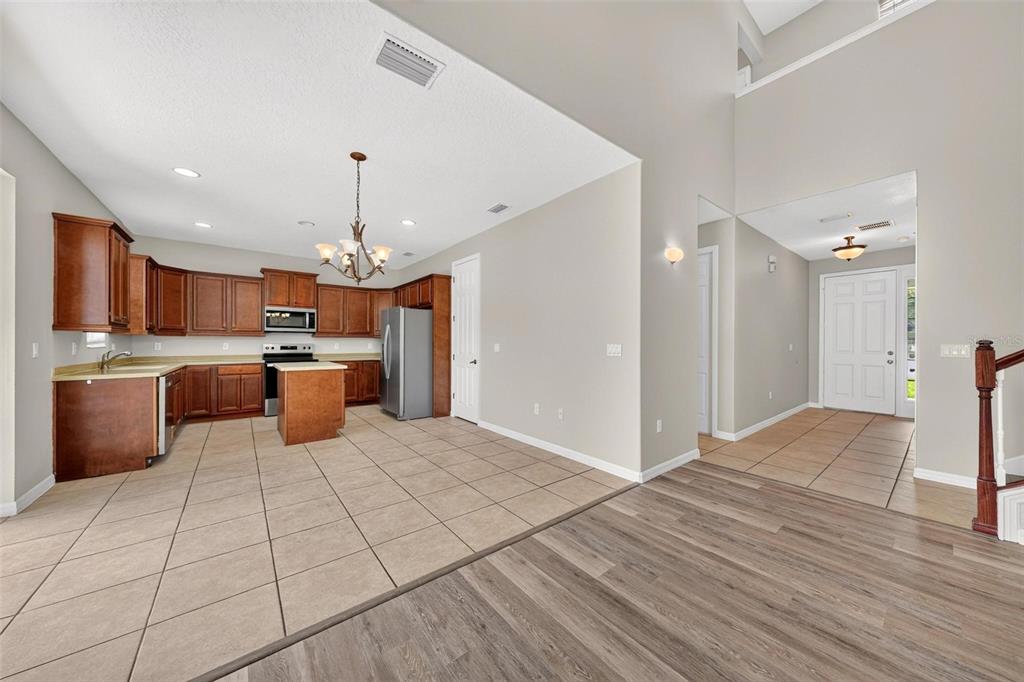 A kitchen with wood cabinets and tile flooring transitions into a living area with wood-look flooring — 3626 OAK BROOK LANE, EUSTIS, FL