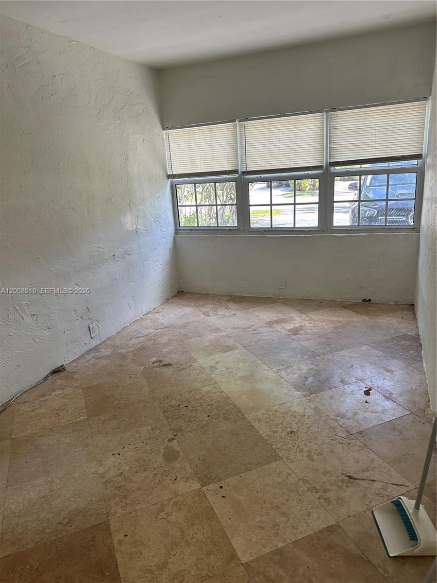 An empty room features textured white walls, large windows with blinds, and stone tile flooring — 1422 Wiley St, Hollywood FL 33020, HOLLYWOOD, FL