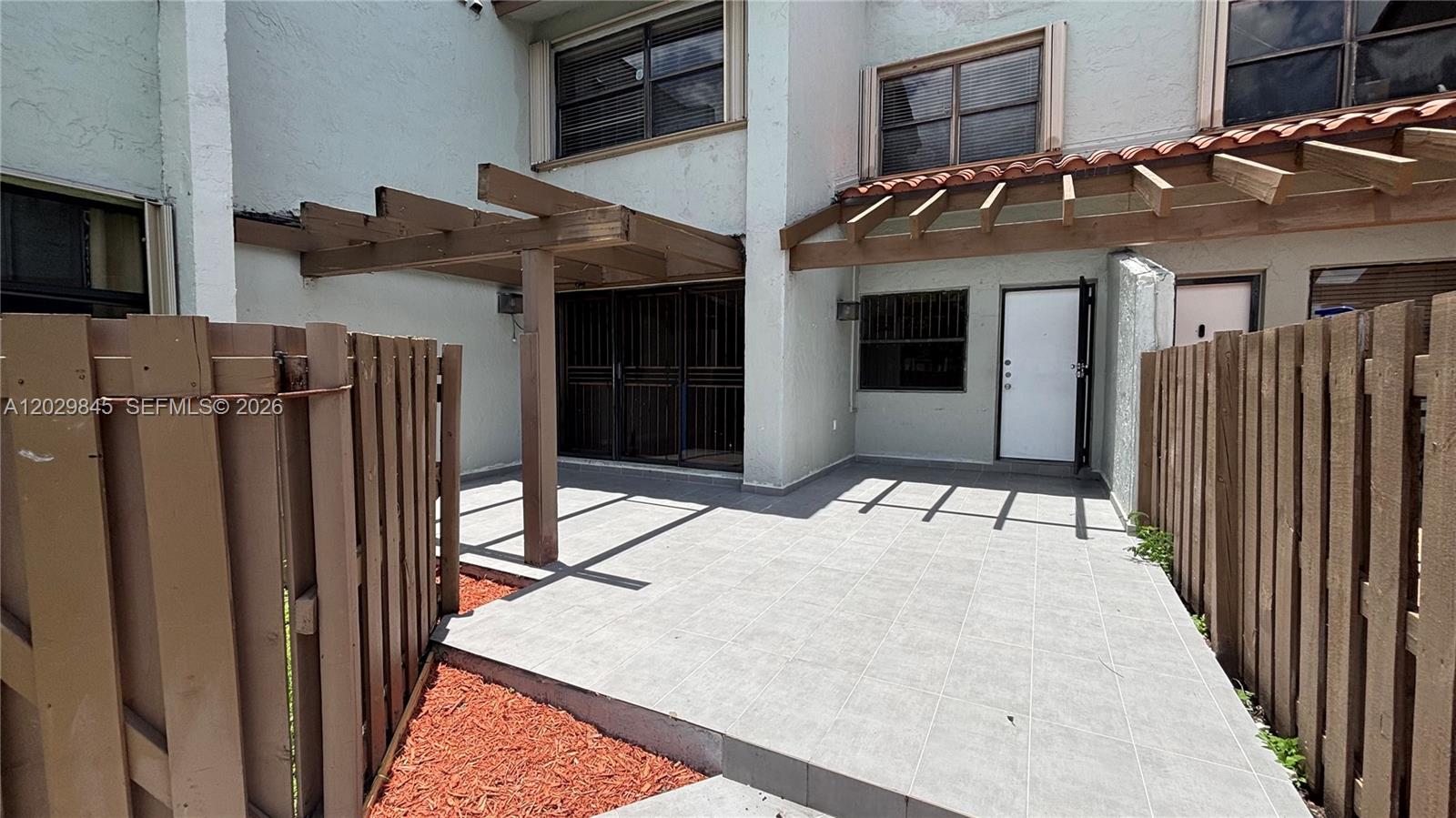 A paved patio area features a wooden pergola, a white door, and wooden privacy fencing — 10303 NW 9th St Cir # 16, Miami FL 33172, MIAMI, FL