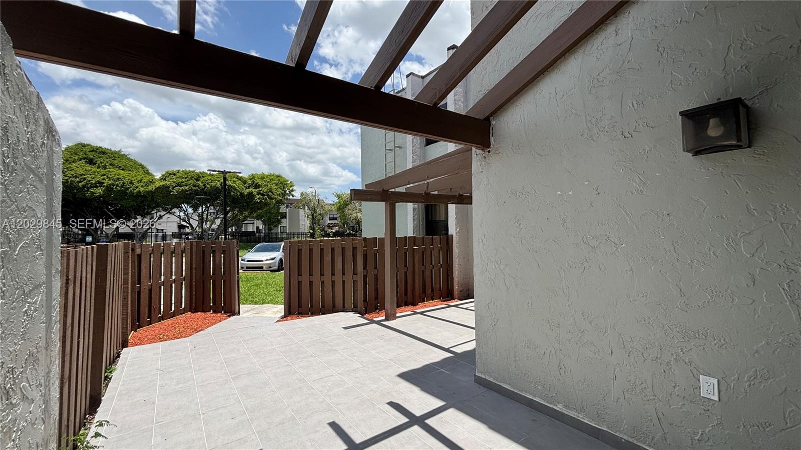 A patio features light gray tile flooring, a wooden pergola, and a wooden privacy fence — 10303 NW 9th St Cir # 16, Miami FL 33172, MIAMI, FL