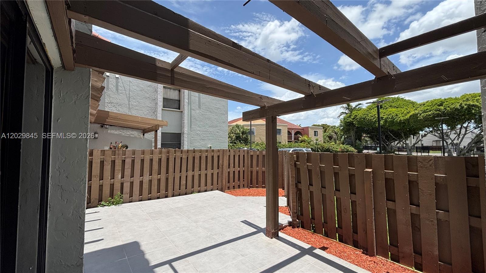 A patio features light gray tiles, a wooden pergola, and a surrounding brown privacy fence — 10303 NW 9th St Cir # 16, Miami FL 33172, MIAMI, FL