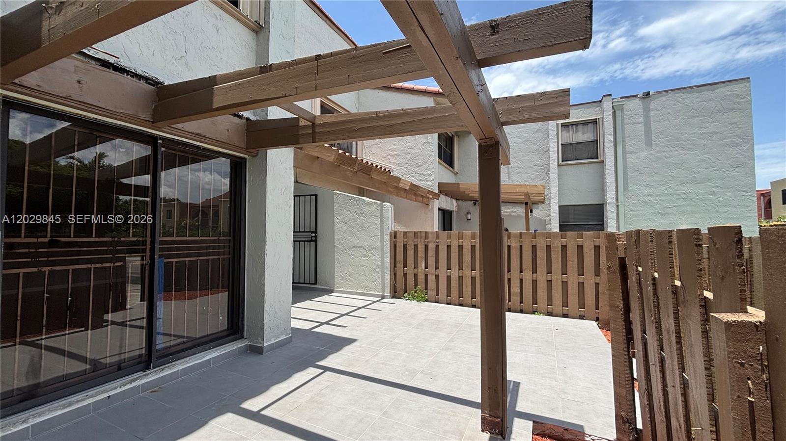 A tiled patio features a wooden pergola structure and a wooden privacy fence — 10303 NW 9th St Cir # 16, Miami FL 33172, MIAMI, FL