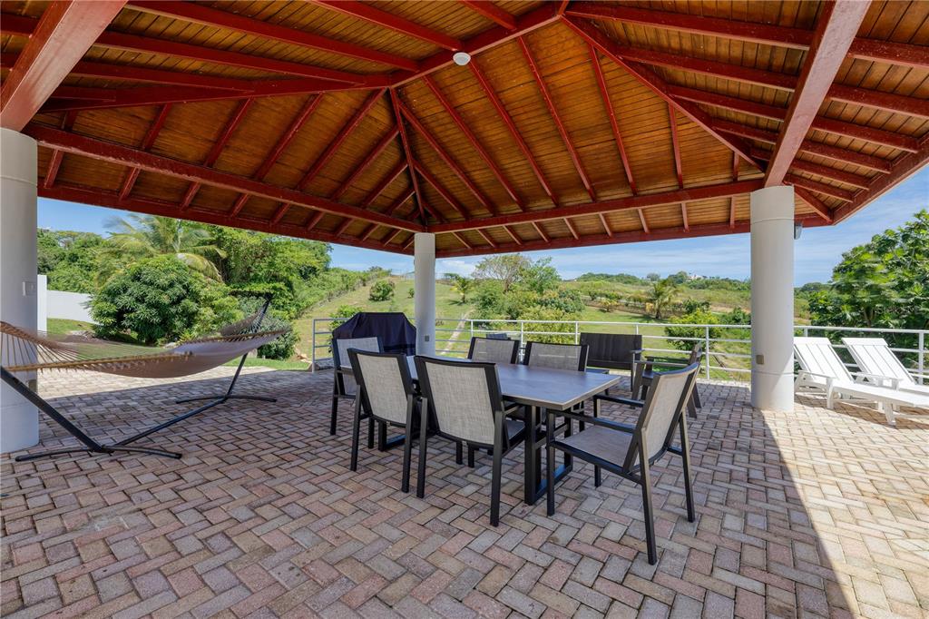 A covered outdoor patio features a dining set, a hammock, and views of a grassy landscape — 94 EL COCAL COUNTRY AND BEACH CLUB, YABUCOA, PR