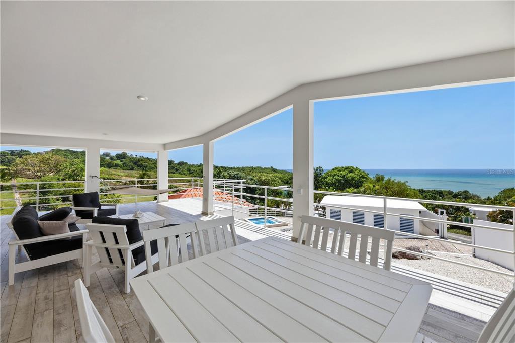 A spacious covered balcony features white furniture, tile flooring, and panoramic ocean and landscape views — 94 EL COCAL COUNTRY AND BEACH CLUB, YABUCOA, PR