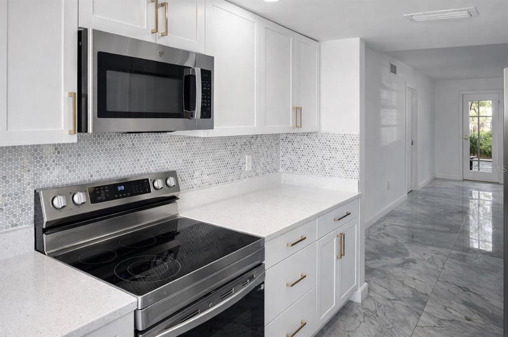 A modern kitchen features white cabinets, stainless steel appliances, quartz countertops, and a mosaic backsplash — 7043 NEW POST DR UNIT 4, NORTH FORT MYERS, FL