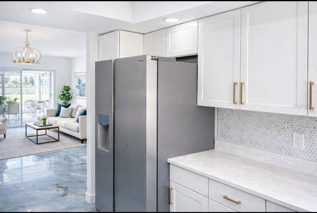 A kitchen with white cabinets and a stainless steel refrigerator opens into a living room — 7043 NEW POST DR UNIT 4, NORTH FORT MYERS, FL