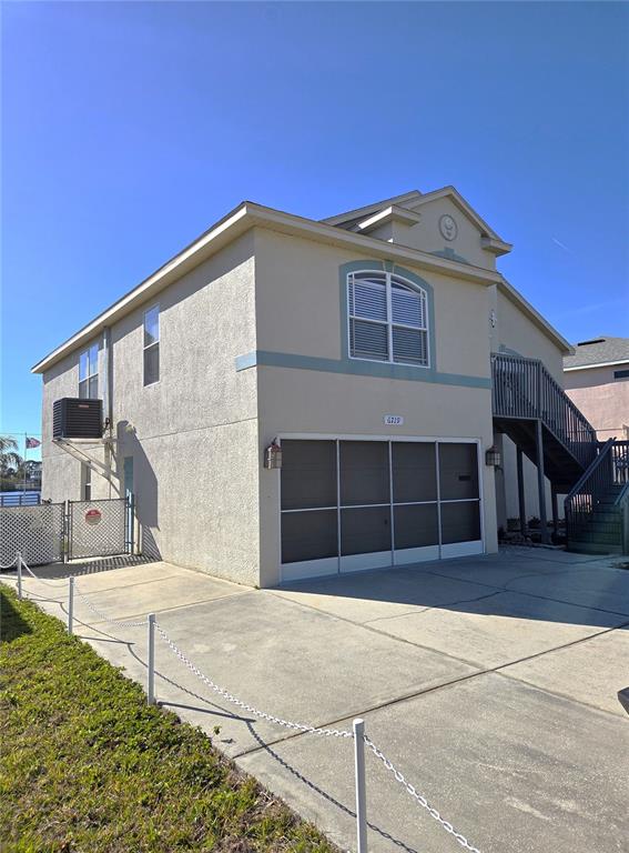 A two-story house with a garage, exterior staircase, and a concrete driveway under a blue sky — 6719 MANOR BEACH, NEW PORT RICHEY, FL