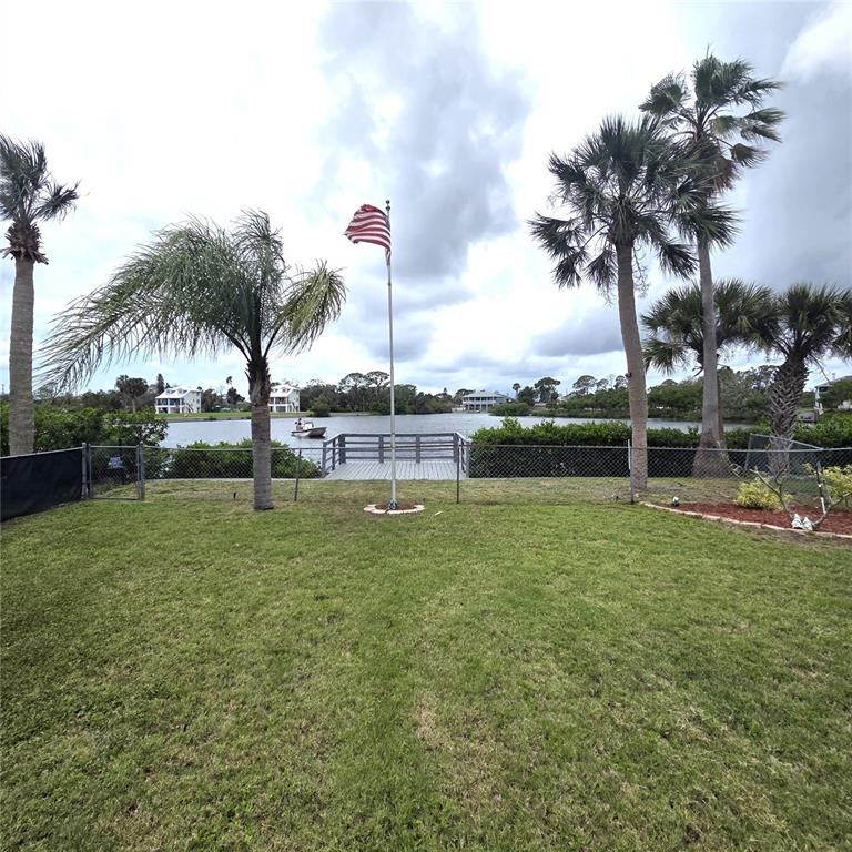 A grassy backyard features a flagpole, a chain-link fence, and a wooden dock overlooking water — 6719 MANOR BEACH, NEW PORT RICHEY, FL