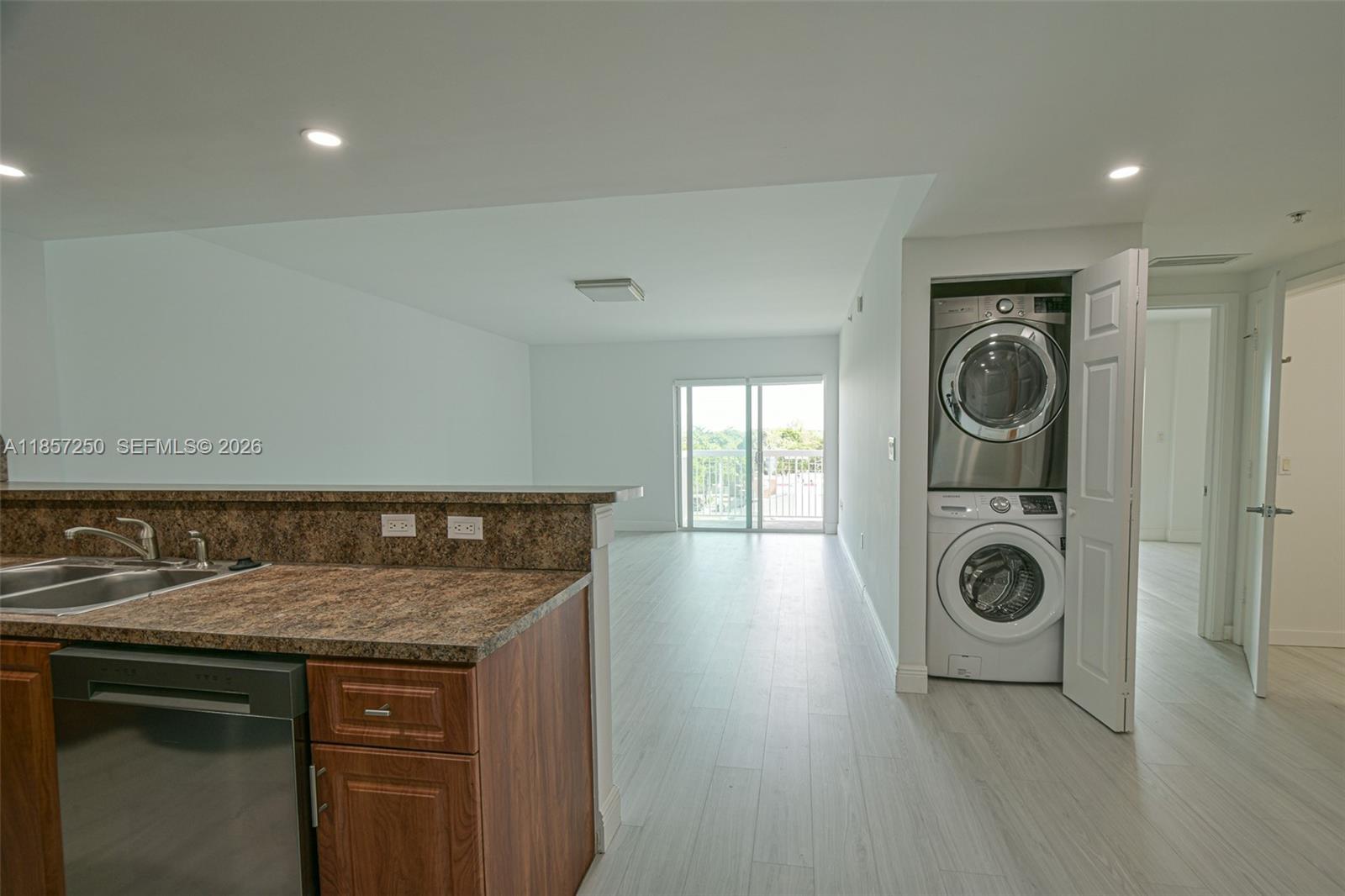 A kitchen with granite countertops overlooks an open living area with a stacked laundry unit — 2740 SW 28th Ter # 603, Miami FL 33133, MIAMI, FL