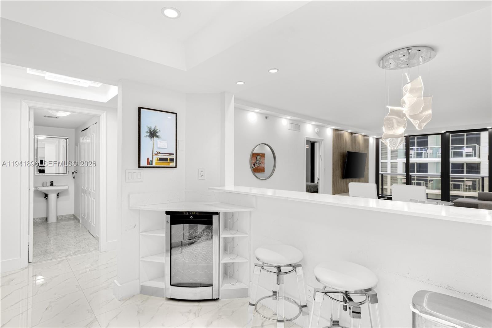 A modern white kitchen features a built-in wine cooler, bar seating, and marble flooring — 9455 Collins Ave # 806, Surfside FL 33154, SURFSIDE, FL