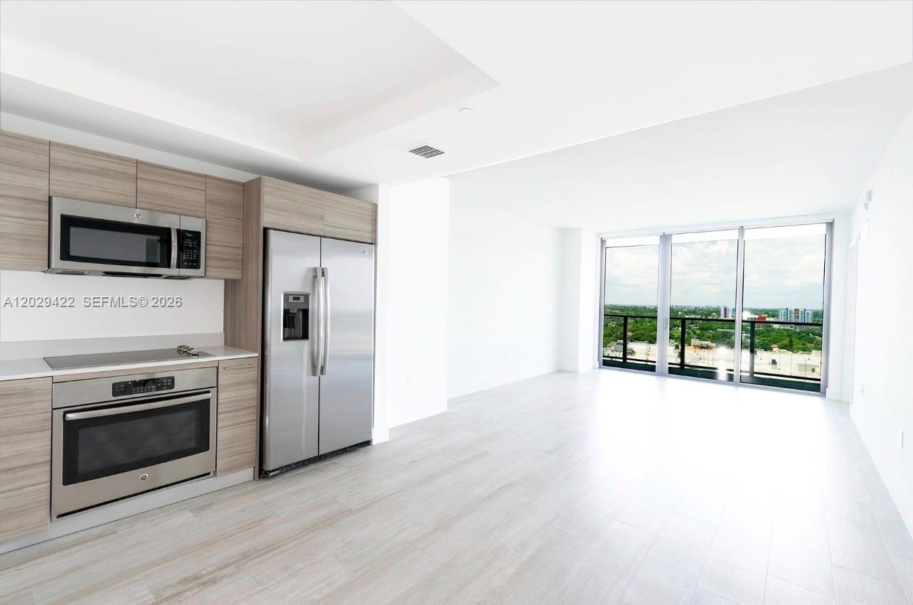 A modern kitchen with stainless steel appliances and light wood cabinets opens to a living area — 121 NE 34th St # 1412, Miami FL 33137, MIAMI, FL