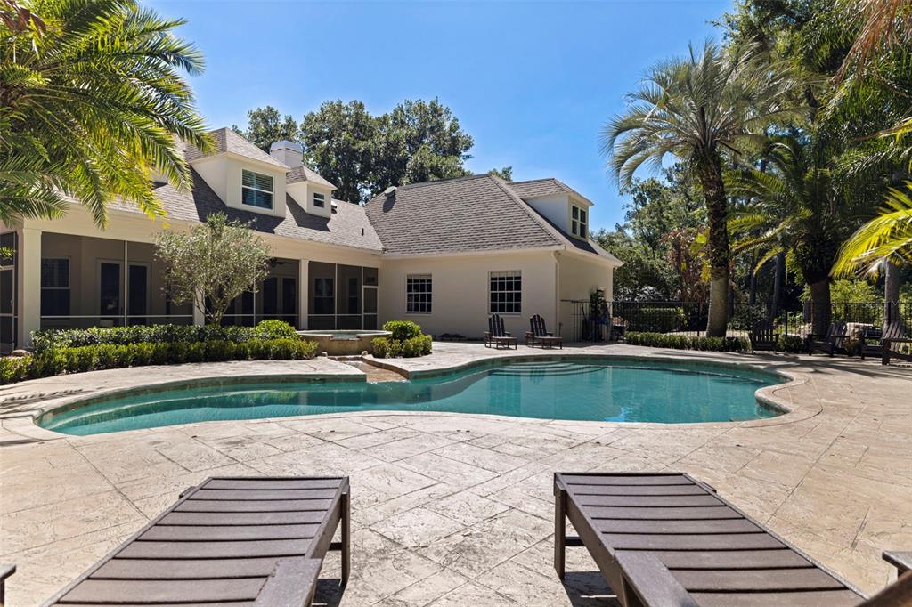 A backyard features a swimming pool, a screened-in patio, and lounge chairs on a stone deck — 6509 STONINGTON DRIVE S, TAMPA, FL