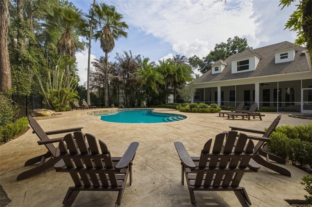 A backyard features a swimming pool, a stone patio, several lounge chairs, and a house — 6509 STONINGTON DRIVE S, TAMPA, FL