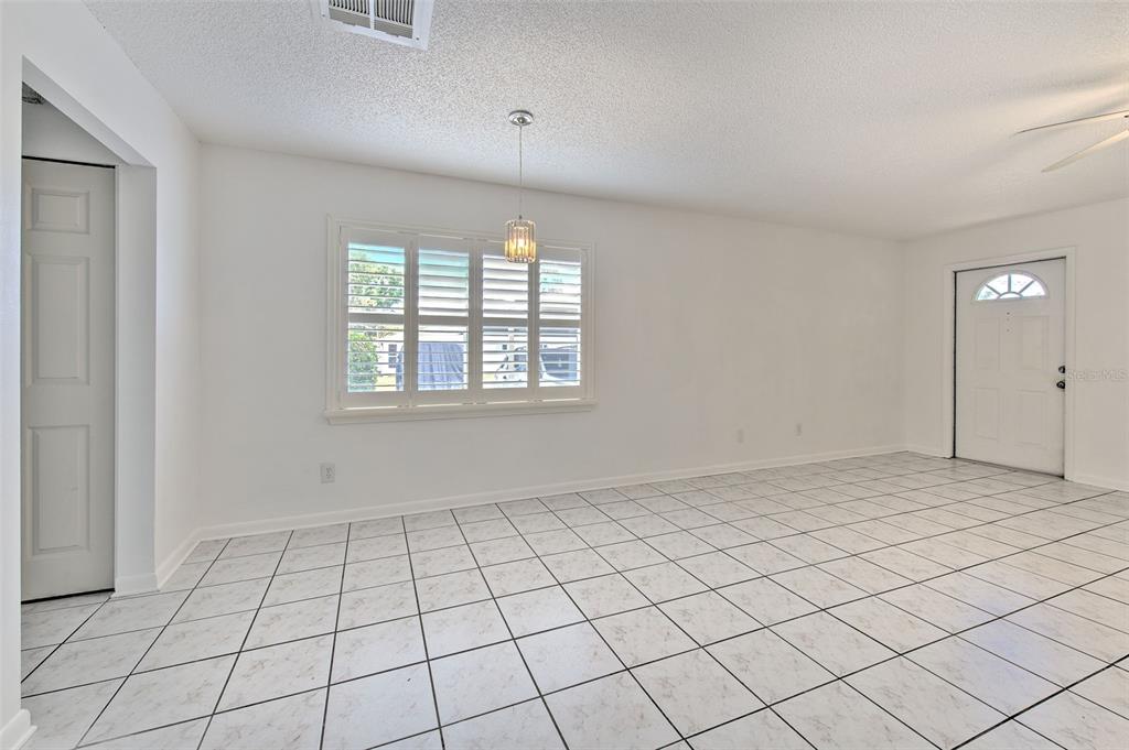 An empty room with white walls, white tile flooring, a window with shutters, and a pendant — 401 DORCHESTER PLACE UNIT 49, SUN CITY CENTER, FL