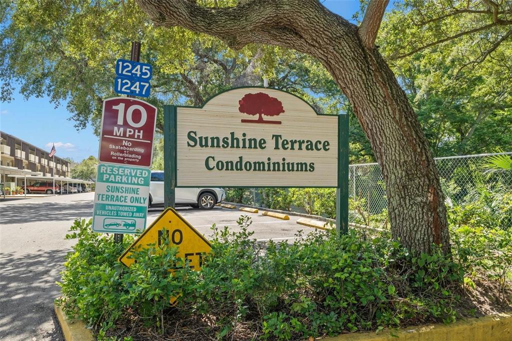 A sign for Sunshine Terrace Condominiums stands near a parking lot and a large tree — 1247 S MARTIN LUTHER KING JR AVENUE UNIT D103, CLEARWATER, FL