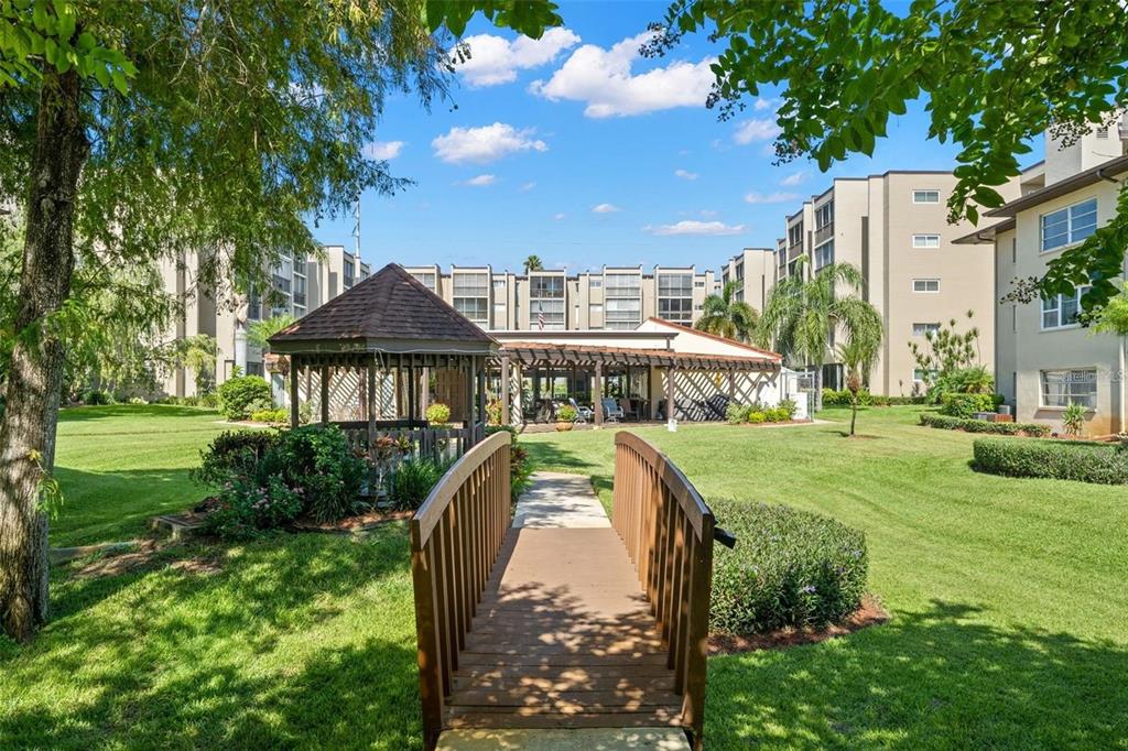A wooden footbridge leads across a grassy lawn toward a gazebo and apartment buildings — 1247 S MARTIN LUTHER KING JR AVENUE UNIT D103, CLEARWATER, FL