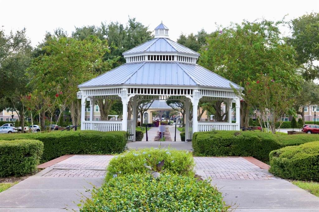 A white wooden gazebo with a metal roof stands in a landscaped courtyard — 6627 QUEENS BOROUGH AVENUE UNIT 108, ORLANDO, FL