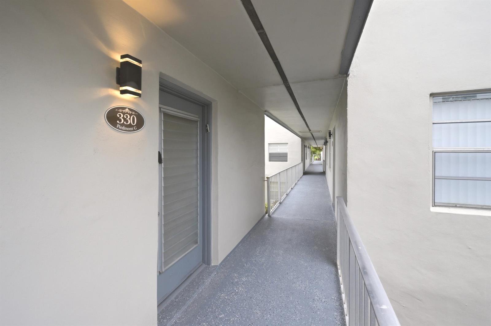 An outdoor apartment hallway features a gray door, a light fixture, and metal railings — 330 Piedmont # 330, Delray Beach FL 33484, DELRAY BEACH, FL