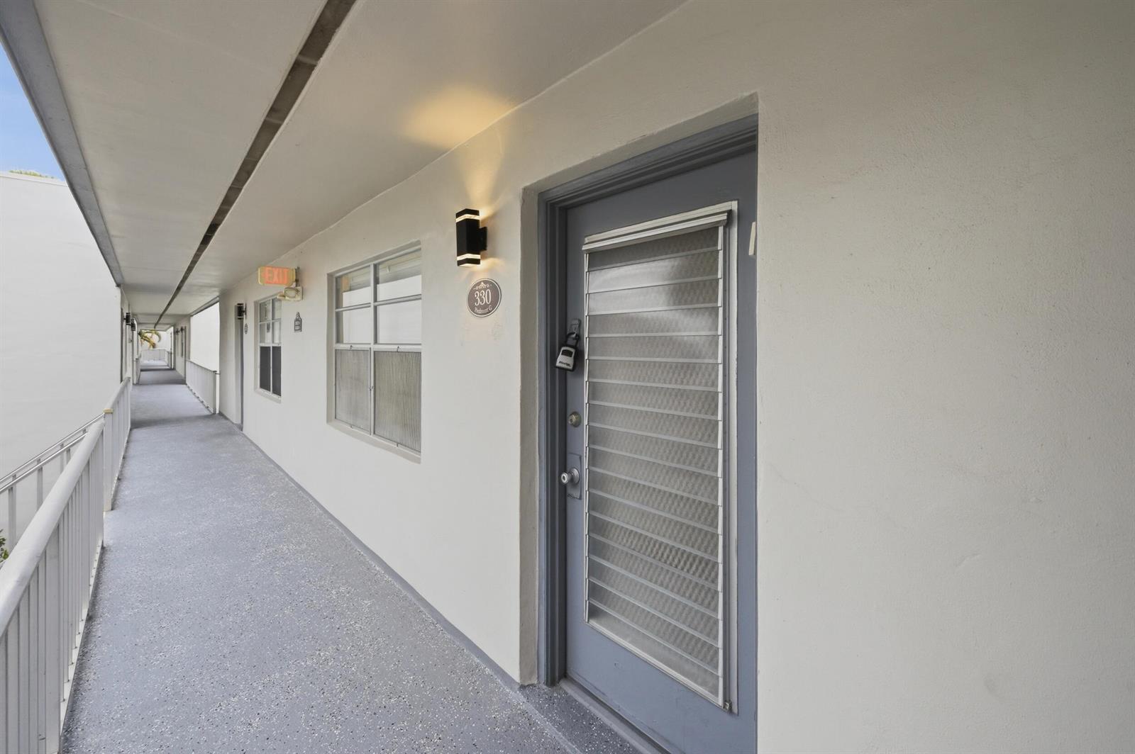 An exterior view of an apartment building hallway with a gray door and windows — 330 Piedmont # 330, Delray Beach FL 33484, DELRAY BEACH, FL