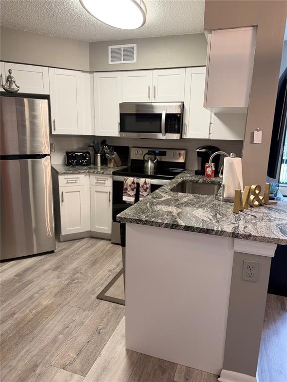 A kitchen features white cabinets, stainless steel appliances, and a granite countertop peninsula — 3814 SOUTHPOINTE DRIVE UNIT 1, ORLANDO, FL