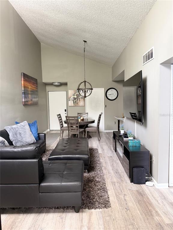 A living room features a vaulted ceiling, wood-look flooring, a black sectional, and dining area — 3814 SOUTHPOINTE DRIVE UNIT 1, ORLANDO, FL