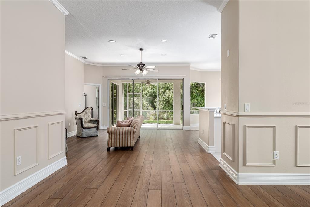A living room with wood-look tile flooring, wainscoting, and sliding glass doors leading to a lanai — 3208 WOODLAND FERN DRIVE, PARRISH, FL