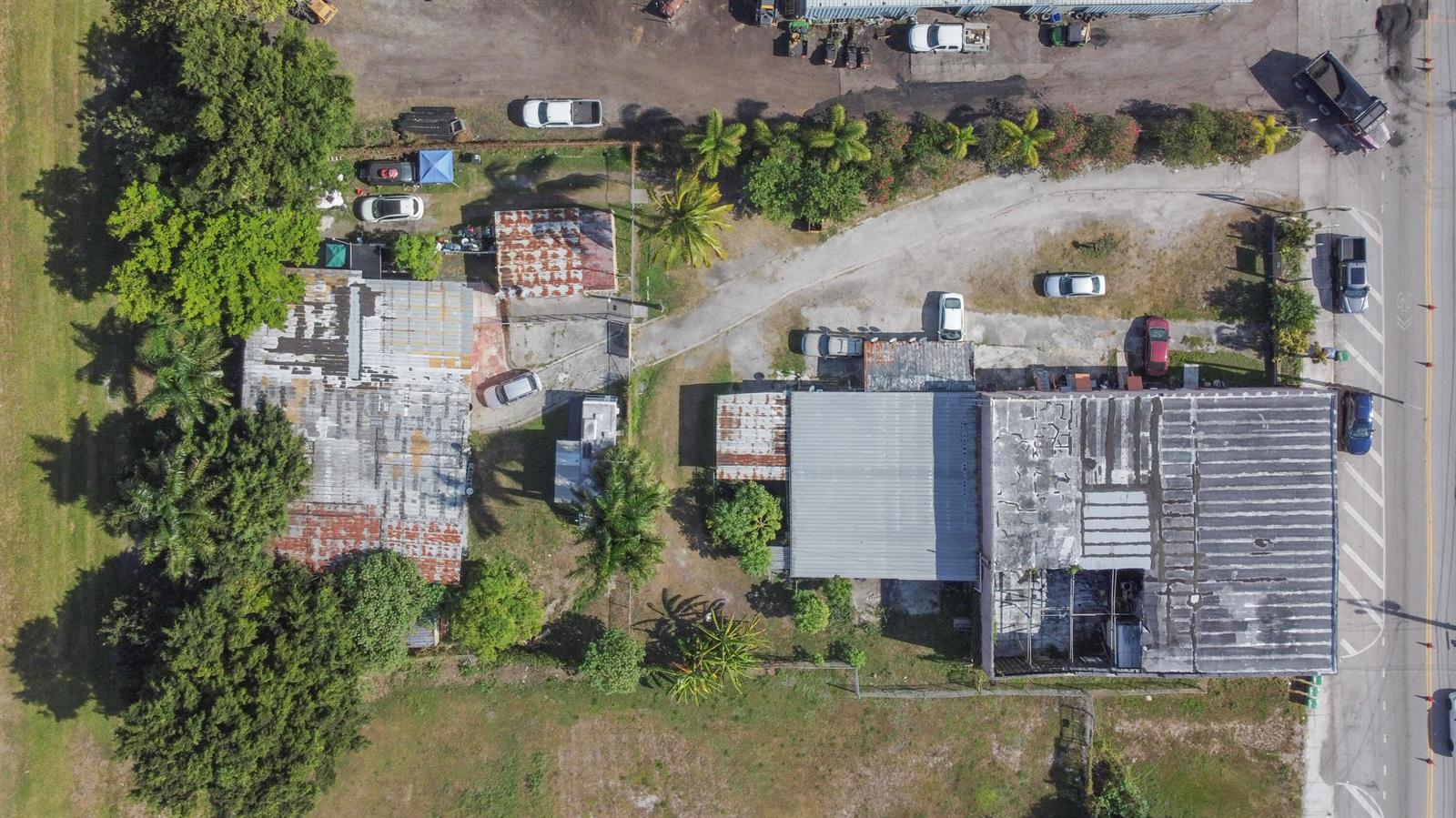 An aerial view shows two industrial buildings with weathered roofs surrounded by trees and parking — 185 E Main Street, Pahokee FL 33476, PAHOKEE, FL