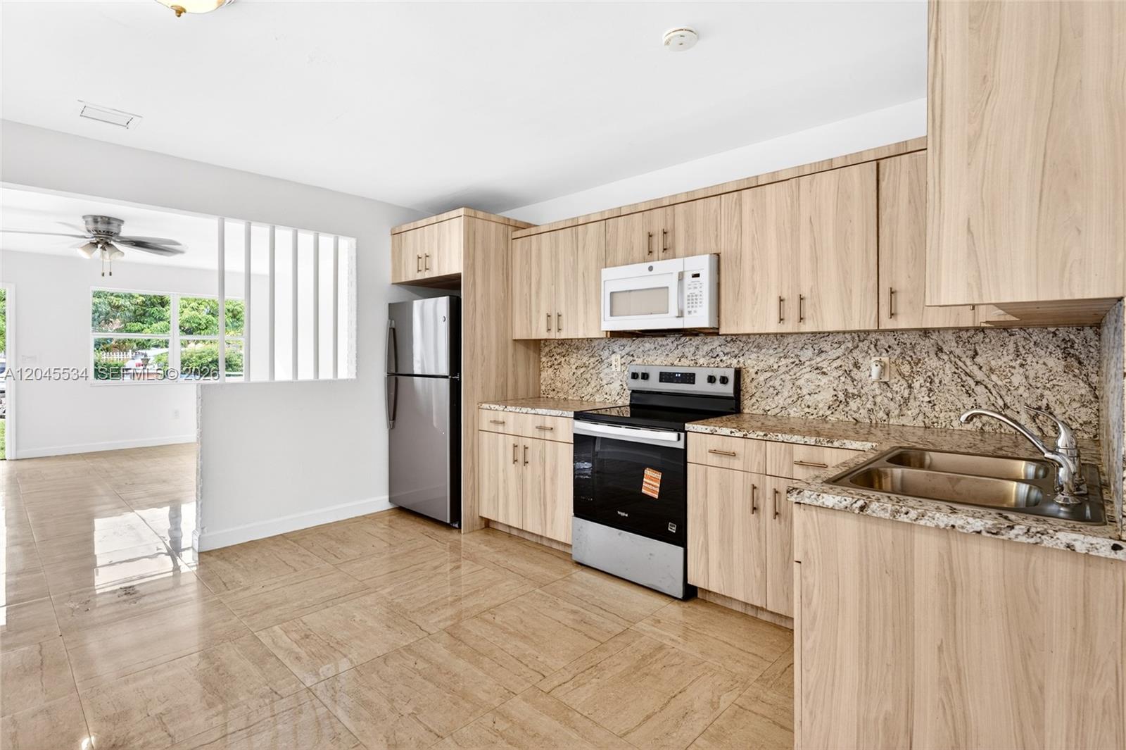 A kitchen features light wood cabinets, granite countertops, stainless steel appliances, and beige tile flooring — 1350 NE 149th St # 2, Miami FL 33161, MIAMI, FL