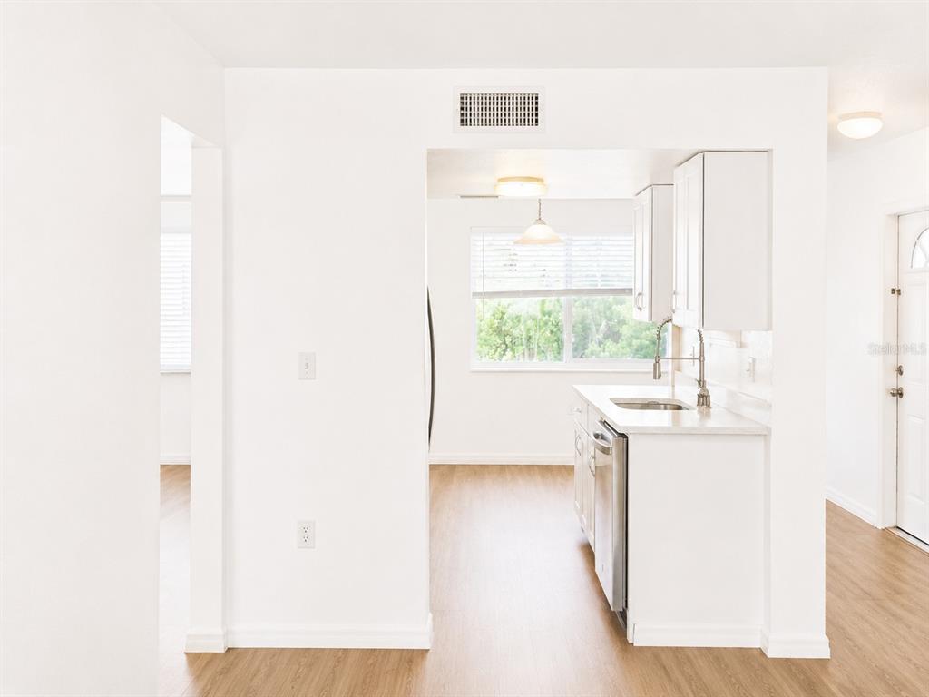 A kitchen with white cabinets and light wood-look flooring viewed from an adjacent room — 5310 26TH STREET W UNIT 1406, BRADENTON, FL