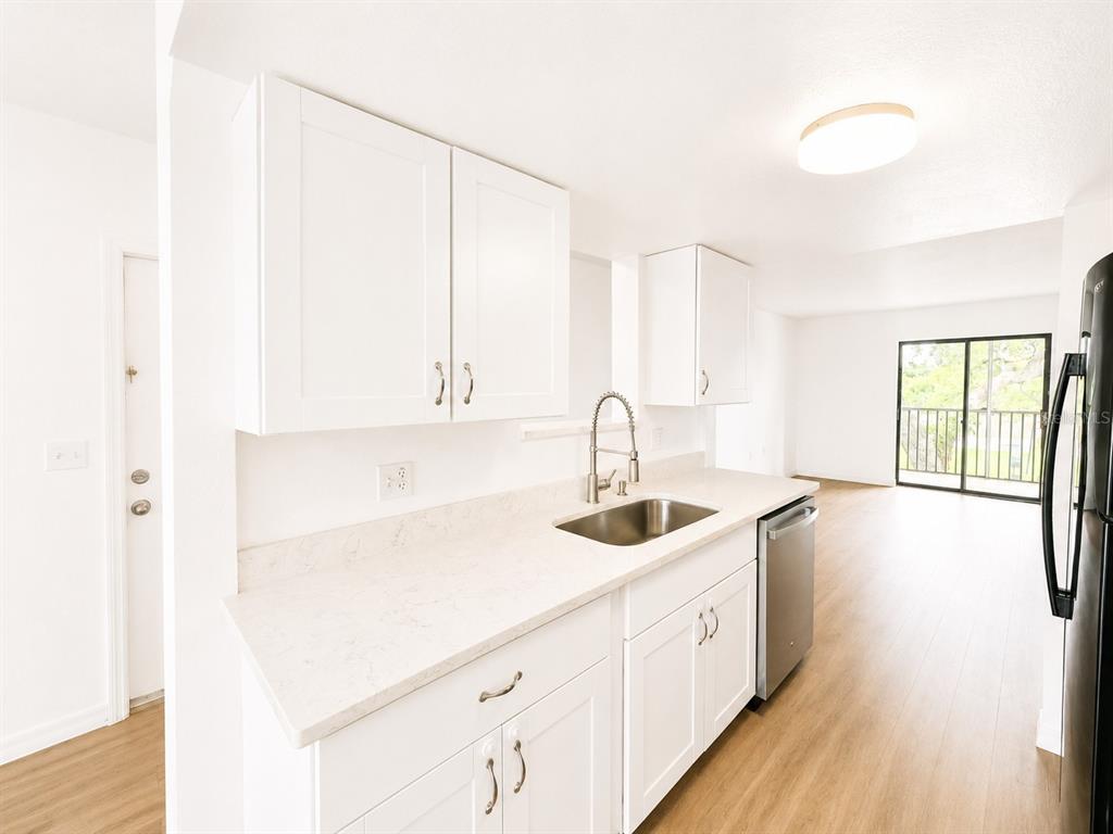 A kitchen features white cabinets, light countertops, a stainless steel sink, and wood-look flooring — 5310 26TH STREET W UNIT 1406, BRADENTON, FL