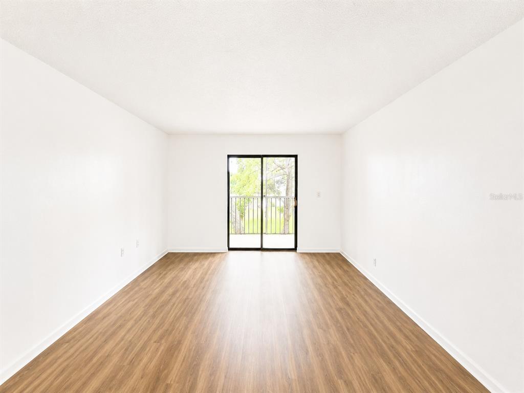 An empty room with light wood-look flooring, white walls, and a sliding glass balcony door — 5310 26TH STREET W UNIT 1406, BRADENTON, FL