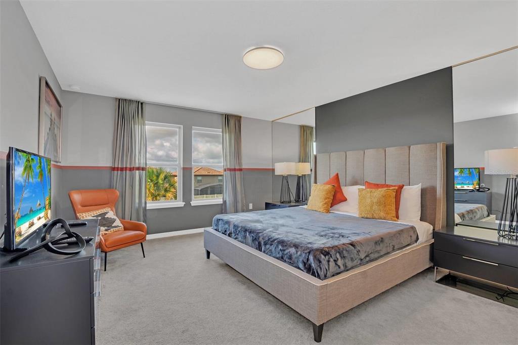 A bedroom features a gray upholstered bed, mirrored wall panels, and an orange accent chair — 8900 SYDNEY AVENUE, KISSIMMEE, FL