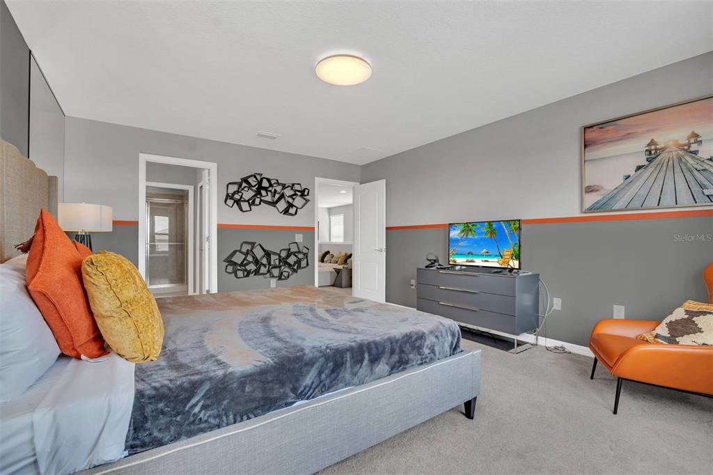 A bedroom features a gray bed, orange accents, a television on a dresser, and wall art — 8900 SYDNEY AVENUE, KISSIMMEE, FL