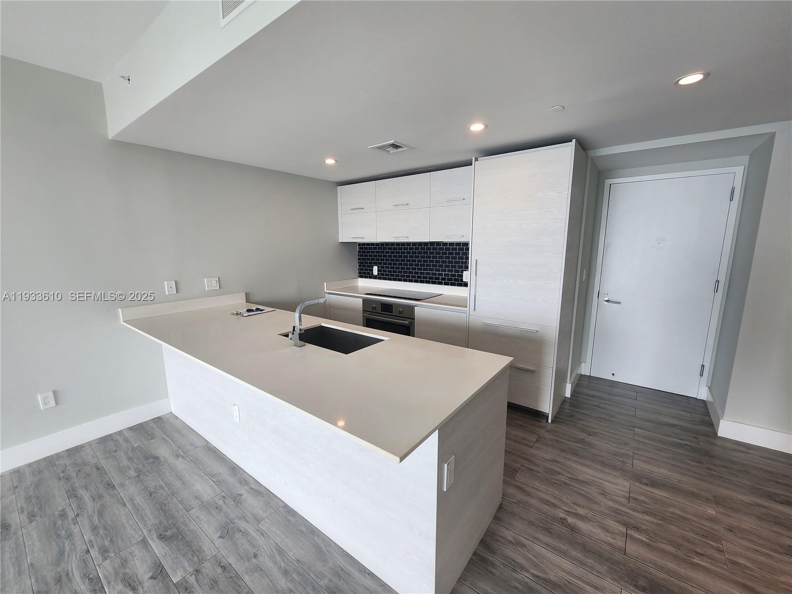 A modern kitchen features a white island, light wood cabinetry, and a black tile backsplash — 1300 S Miami Ave # 3502, Miami FL 33130, MIAMI, FL