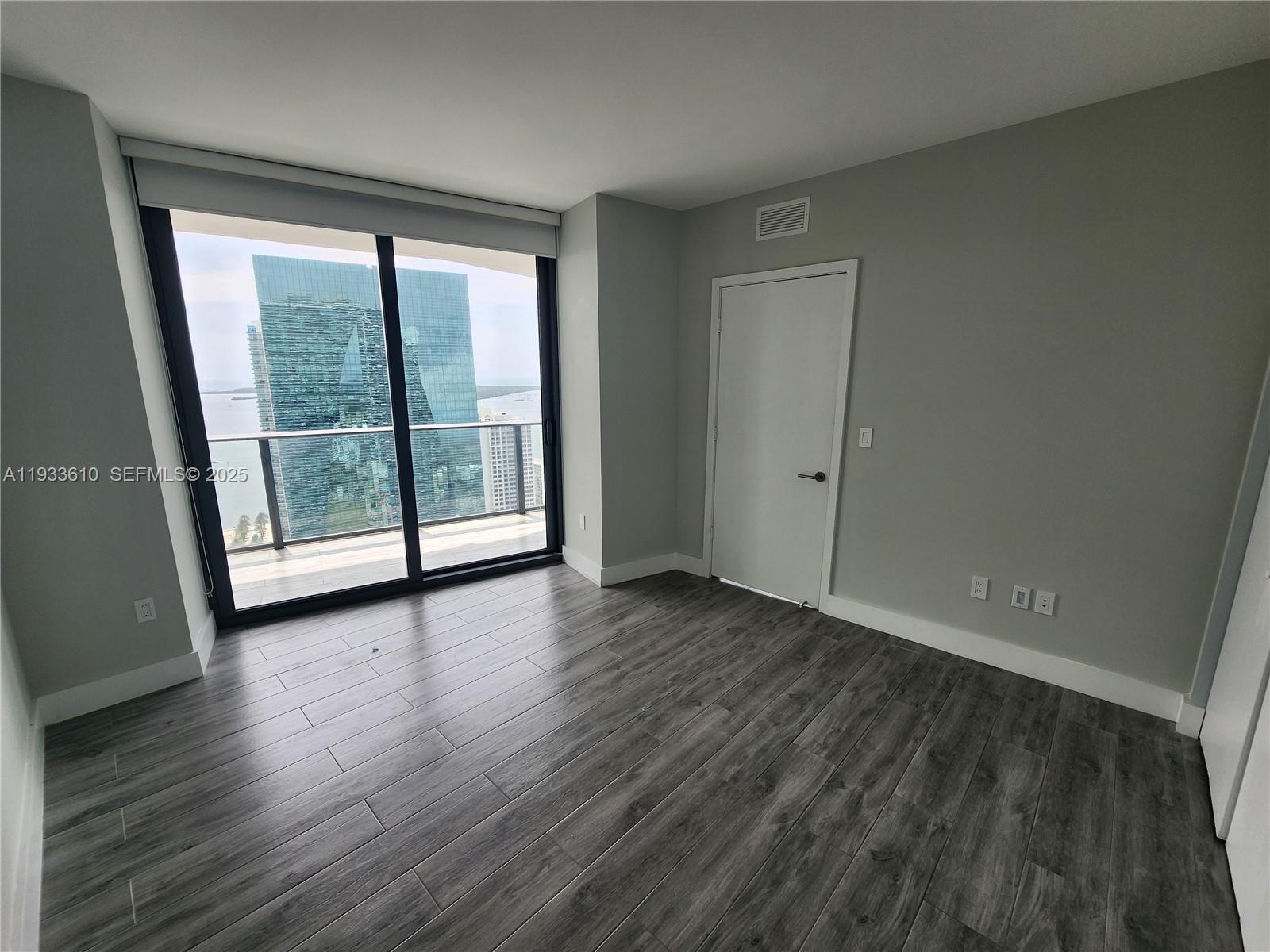 An empty room features gray wood-look flooring, light gray walls, and a sliding glass balcony door — 1300 S Miami Ave # 3502, Miami FL 33130, MIAMI, FL